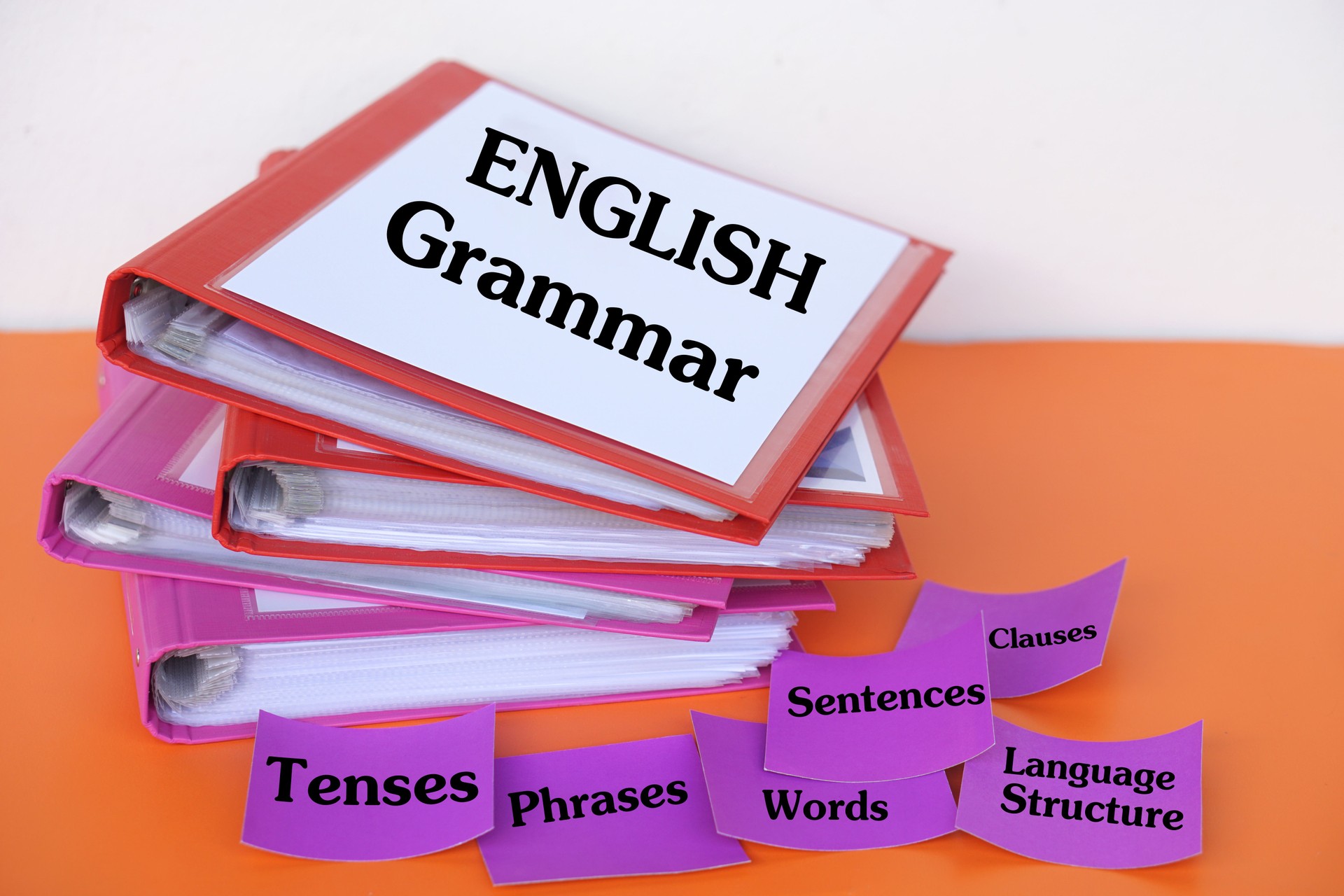 Stack of colorful binders labeled "English Grammar" with flashcards showing Tenses, Words, Sentences, Phrases, Clauses, and Language Structure. Educational material for grammar learning and teaching.